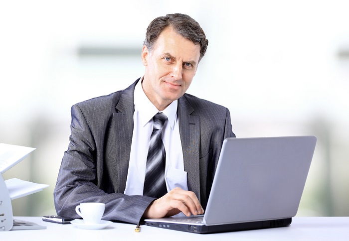man in his 50s in a gray suit working on his laptop